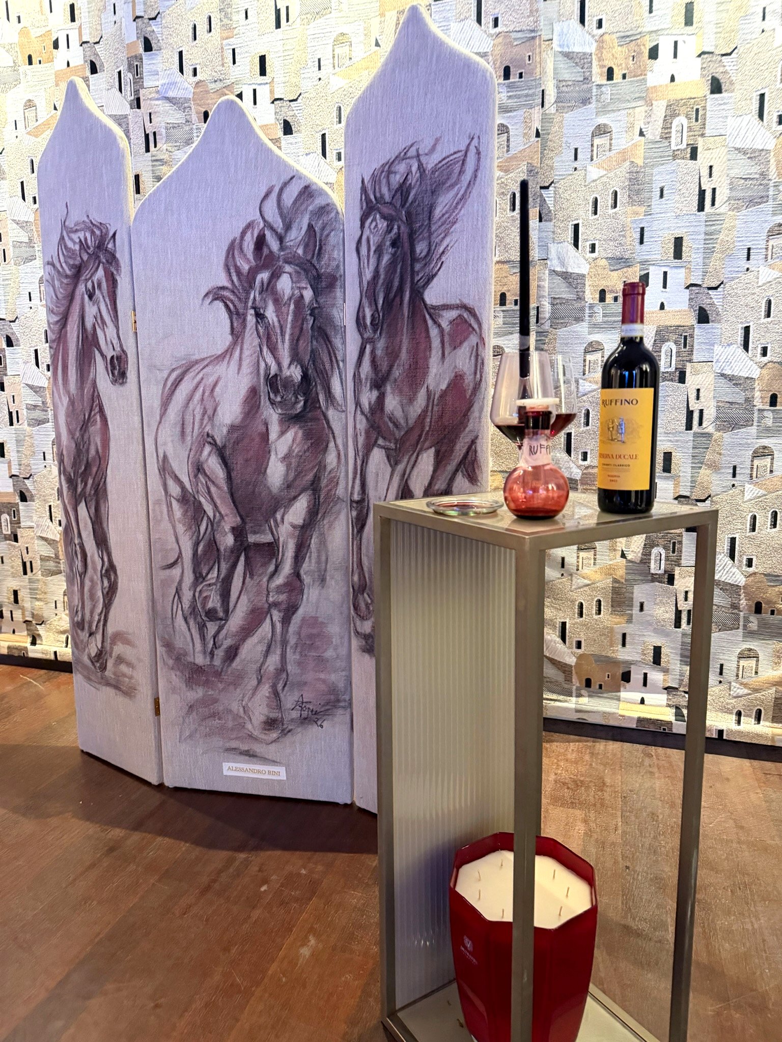 Parawan z trzema końmi namalowanymi winem przez Elisabettę Rogai, obok butelka Ruffino Riserva Ducale Chianti Classico